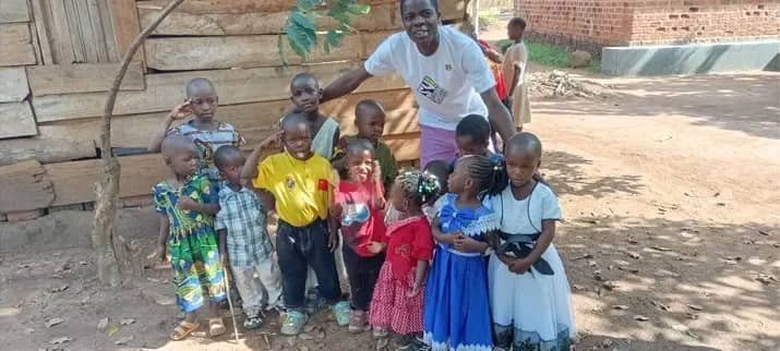 Children and a caregiver standing between wooden and brick buildings